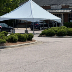 White tent set up in a parking lot outside a brick building, surrounded by greenery.