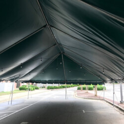 Inside view of a large green tent set up over a paved road, with visible string lights.