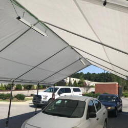 White canopy tent covering multiple parked cars in an outdoor area, with trees and buildings in the background.