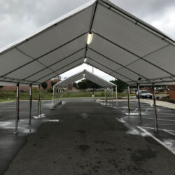 A row of large white tents set up over an empty parking lot on a cloudy day.