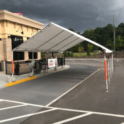 A white tent structure set up over a drive-thru lane next to a building on an overcast day.