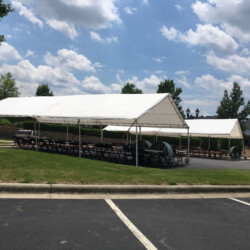 Two large white tents set up in a parking lot with rows of chairs underneath, on a sunny day with scattered clouds.