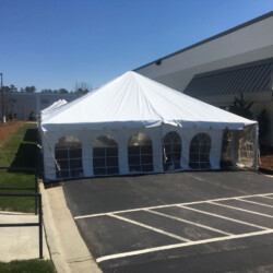 A large white tent with arched windows is set up in an asphalt parking lot beside a modern building.