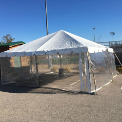 Large outdoor tent with clear plastic walls set up on a paved area under a clear blue sky.