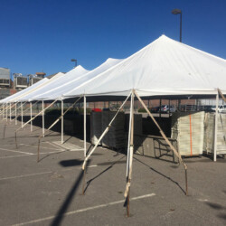Large white tents set up in a parking lot with stacked tables underneath on a clear day.