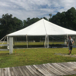 A large white tent is set up on a grassy area, with a person walking nearby and trees in the background.