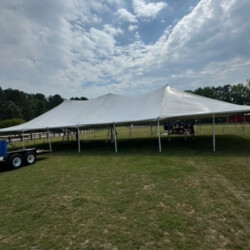 Large white event tent set up on a grassy field, with a trailer nearby and cloudy sky in the background.
