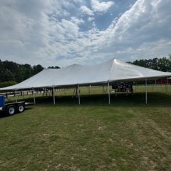 Large white event tent set up on a grassy field, with a trailer nearby and cloudy sky in the background.