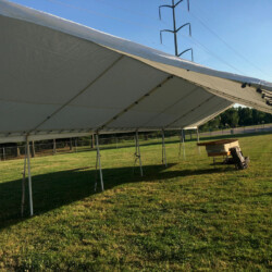 A large white tent on a grassy field, with stacks of folded tables and chairs underneath.