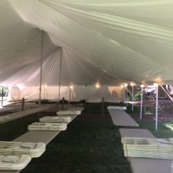 Inside view of a large outdoor tent with folding tables and chairs neatly arranged on the grass.