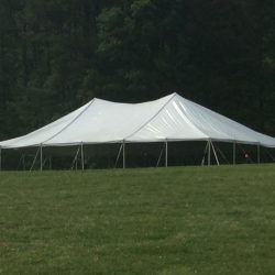 Large white tent set up on a grassy field with trees in the background.