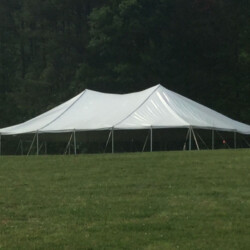 Large white tent set up on a grassy field with trees in the background.
