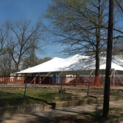 Large white tent in a fenced-off area with surrounding trees and clear skies.