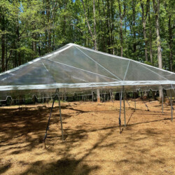 A clear plastic canopy tent is set up in a wooded area with trees and sunlight filtering through.