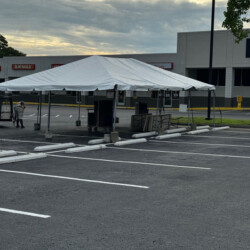 A large white tent set up in an empty parking lot with nearby buildings in the background.