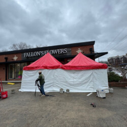 A person takes photos of a structure with red and white canopies outside a flower shop under a cloudy sky.
