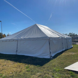 White event tent set up on grassy area under a clear blue sky with sunlight streaming from the top right corner.