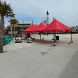 Red tents on an empty beach promenade, with a lighthouse and palm trees in the background.