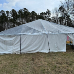 Large white canopy tent with transparent roof, set up on grassy area near trees. A partially open entry flap is visible.