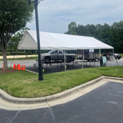 White canopy with a pickup truck underneath, set up in a parking lot with traffic cones and a nearby streetlamp.