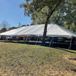 Large white event tent set up outdoors on a grassy area with trees and clear blue sky in the background.