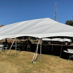 White canopy tent set up on grass with folding tables and chairs underneath; a truck is parked nearby.