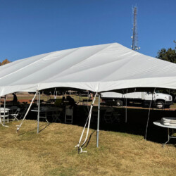 White canopy tent set up on grass with folding tables and chairs underneath; a truck is parked nearby.